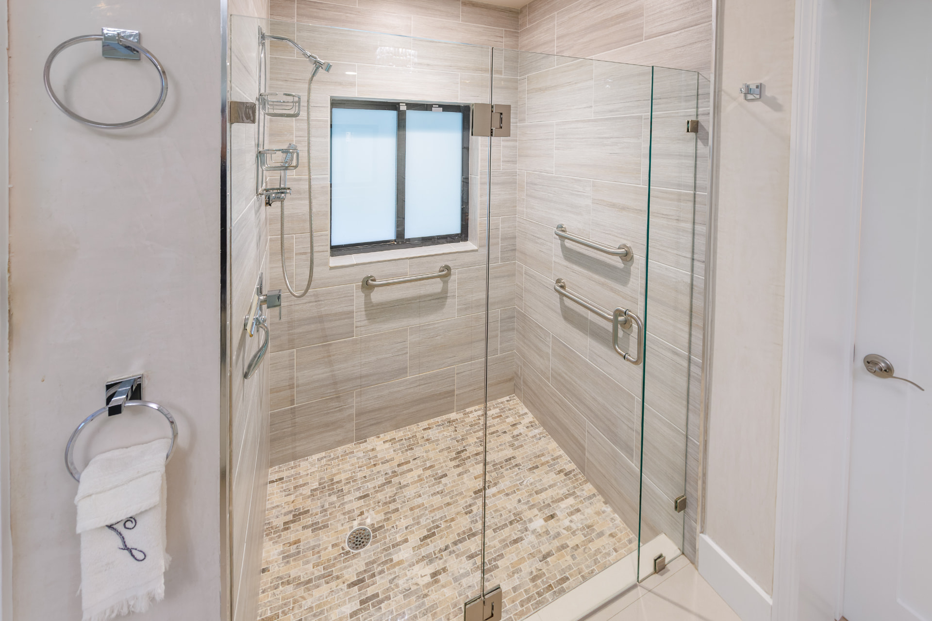 Walk-in glass shower with pebble-tile floor and dual fixtures