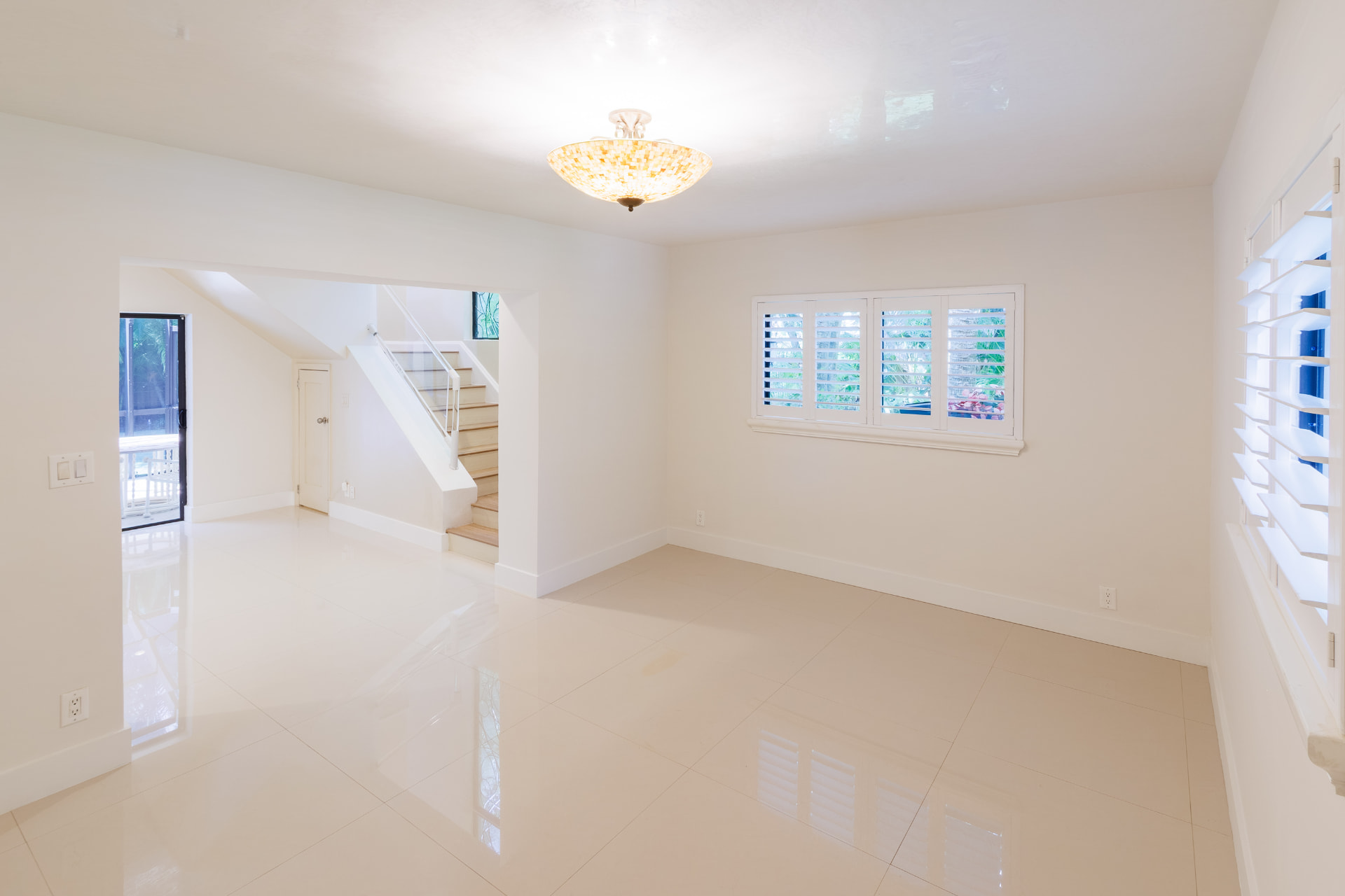 Living room with mosaic-glass chandelier, staircase and polished tile floors